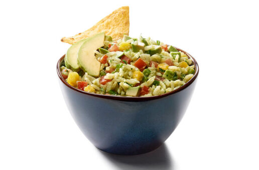 Bowl filled with avocado and mango rice dip with diced tomatoes, avocado chunks and crunchy tortilla chips