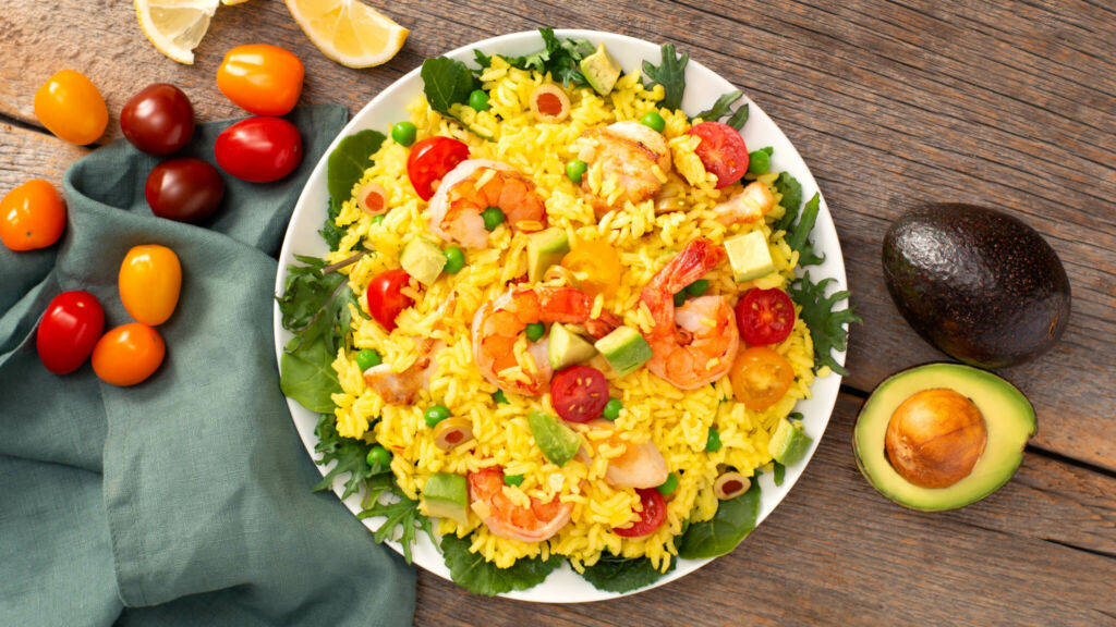 White bowl with paella salad, diced avocados, cherry tomatoes, shrimp, chicken and olives