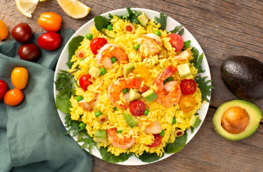 White bowl with paella salad, diced avocados, cherry tomatoes, shrimp, chicken and olives